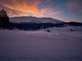 snow covered field near mountain under cloudy sky during daytime