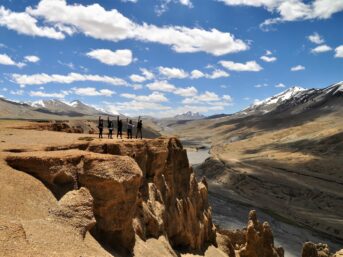 people walking on brown dirt road near gray mountains under blue and white sunny cloudy sky